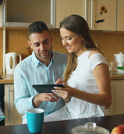 A smiling couple at their kitchen counter looking at a tablet together